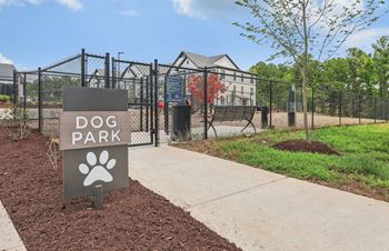 A dog park sign in front of a fence and a dog